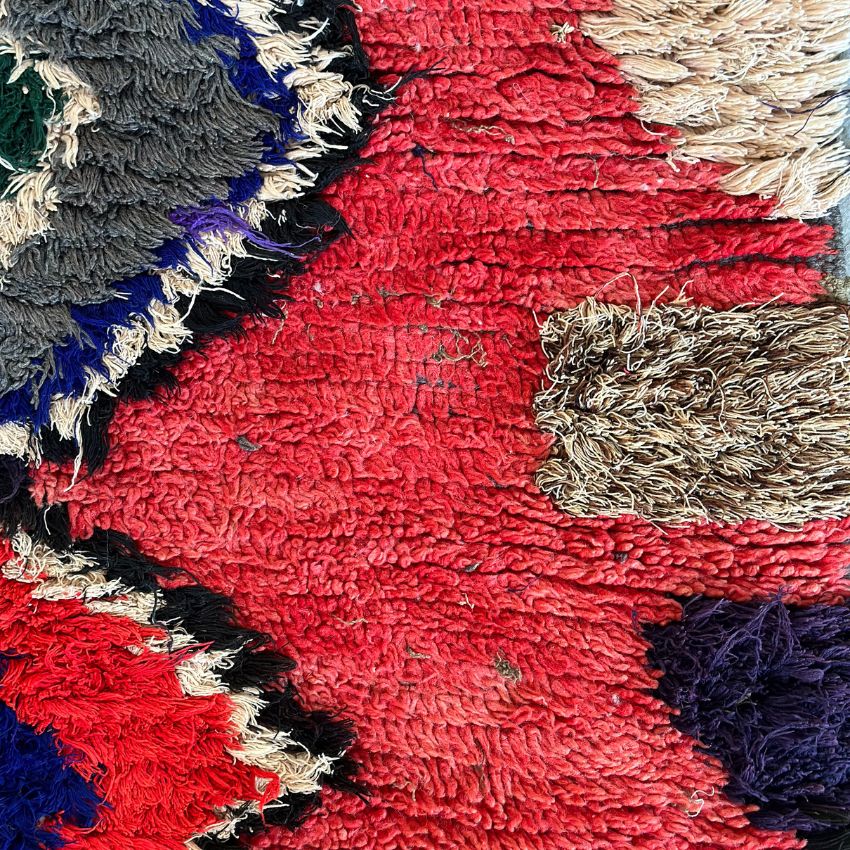 Handwoven Moroccan Boucherouite rug with vibrant geometric diamond motifs, featuring red, violet, green, and cream colors. Crafted by Berber artisans using sustainable recycled materials and wool, ideal for bohemian, eclectic, or modern interiors. Unique cultural design with symbolic motifs from the High Atlas Mountains of Morocco. Photo of close up view of wool pile and texture. 