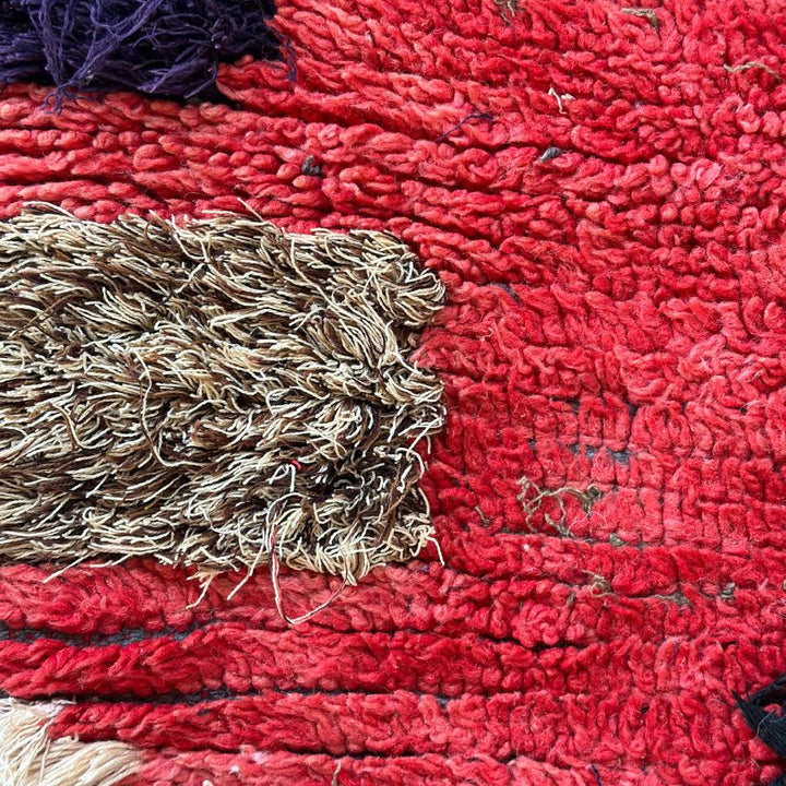 Handwoven Moroccan Boucherouite rug with vibrant geometric diamond motifs, featuring red, violet, green, and cream colors. Crafted by Berber artisans using sustainable recycled materials and wool, ideal for bohemian, eclectic, or modern interiors. Unique cultural design with symbolic motifs from the High Atlas Mountains of Morocco. Photo of close up view of wool pile and texture. 