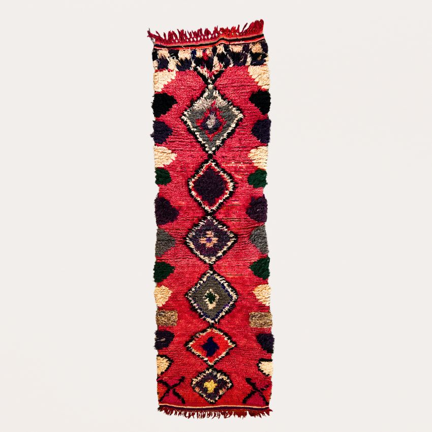 Handwoven Moroccan Boucherouite rug with vibrant geometric diamond motifs, featuring red, violet, green, and cream colors. Crafted by Berber artisans using sustainable recycled materials and wool, ideal for bohemian, eclectic, or modern interiors. Unique cultural design with symbolic motifs from the High Atlas Mountains of Morocco.