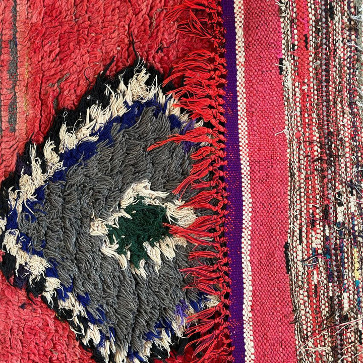 Handwoven Moroccan Boucherouite rug with vibrant geometric diamond motifs, featuring red, violet, green, and cream colors. Crafted by Berber artisans using sustainable recycled materials and wool, ideal for bohemian, eclectic, or modern interiors. Unique cultural design with symbolic motifs from the High Atlas Mountains of Morocco. Photo of close up view of tassels.